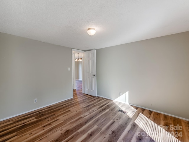 empty room featuring hardwood / wood-style floors, a textured ceiling, and a notable chandelier