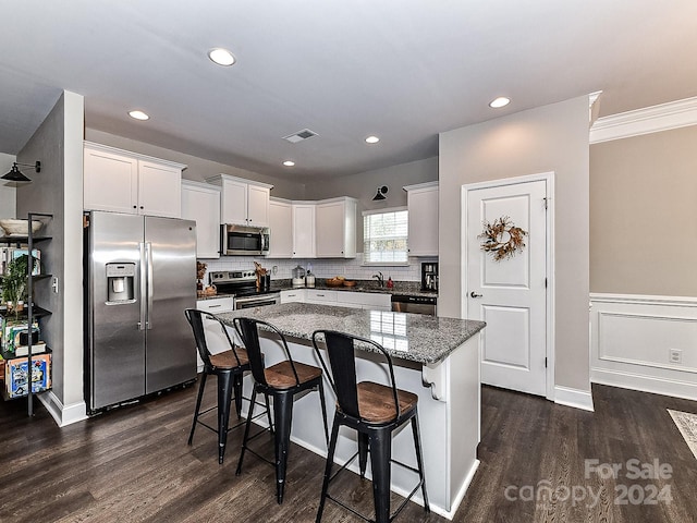 kitchen featuring a breakfast bar, a center island, appliances with stainless steel finishes, dark hardwood / wood-style flooring, and white cabinetry