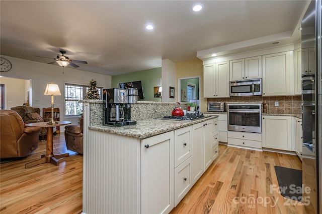 kitchen featuring appliances with stainless steel finishes, open floor plan, light wood-style flooring, and decorative backsplash