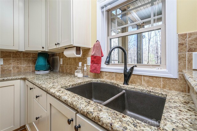 kitchen featuring light stone countertops, tasteful backsplash, white cabinetry, and a sink