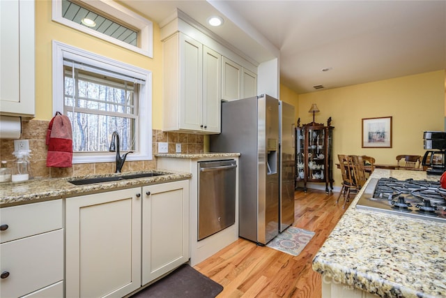 kitchen featuring a sink, white cabinetry, appliances with stainless steel finishes, light wood-type flooring, and decorative backsplash