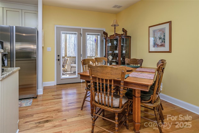 dining area with light wood-type flooring, visible vents, and baseboards