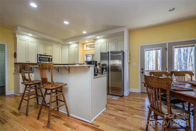 kitchen featuring a healthy amount of sunlight, light wood-style flooring, stainless steel appliances, and a kitchen breakfast bar