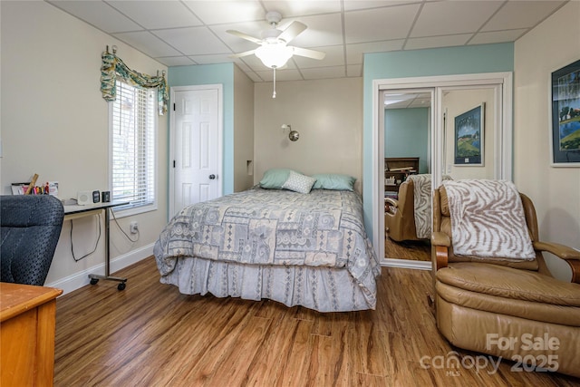 bedroom with a paneled ceiling, a ceiling fan, baseboards, and wood finished floors