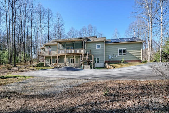 rear view of property with a deck, roof mounted solar panels, stairway, and aphalt driveway