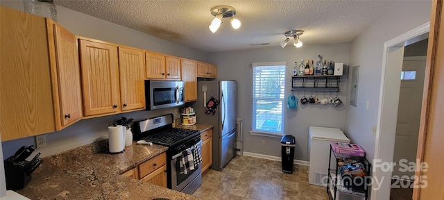 kitchen with stainless steel appliances, a textured ceiling, and dark stone countertops