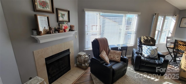 sitting room with a tile fireplace, lofted ceiling, a healthy amount of sunlight, and wood-type flooring