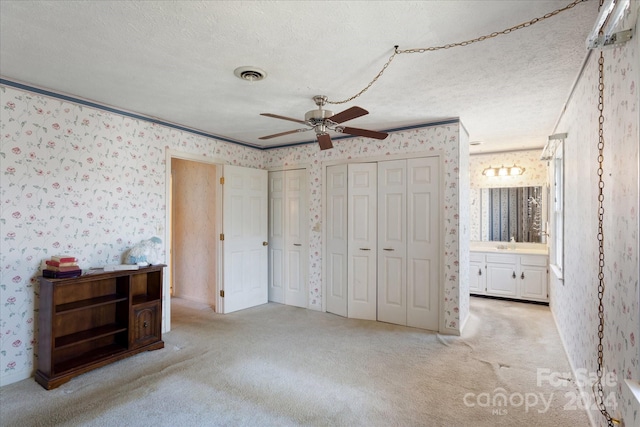 unfurnished bedroom with ensuite bath, ceiling fan, a textured ceiling, light carpet, and two closets