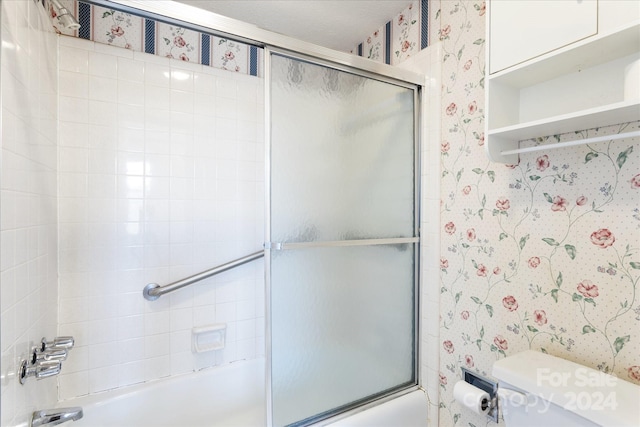 bathroom with toilet and bath / shower combo with glass door