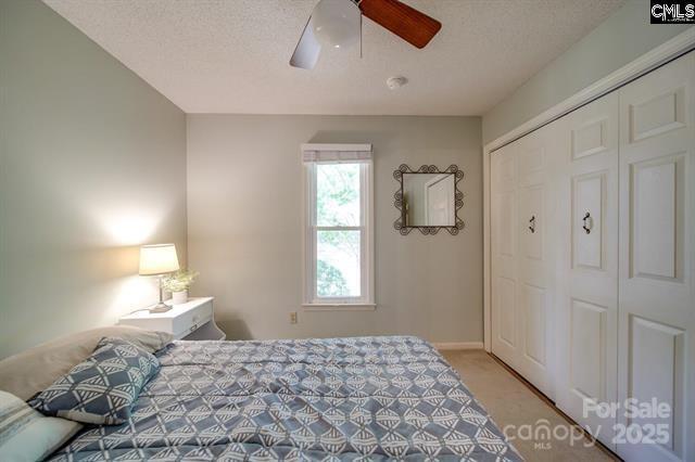 bedroom featuring light carpet, a textured ceiling, a ceiling fan, and a closet