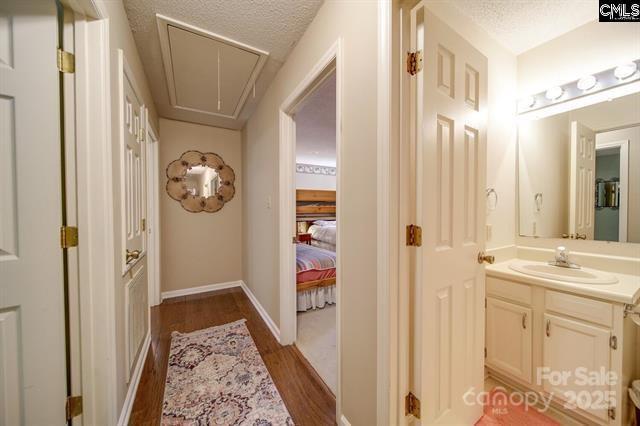 hallway with dark wood-style floors, attic access, a sink, a textured ceiling, and baseboards