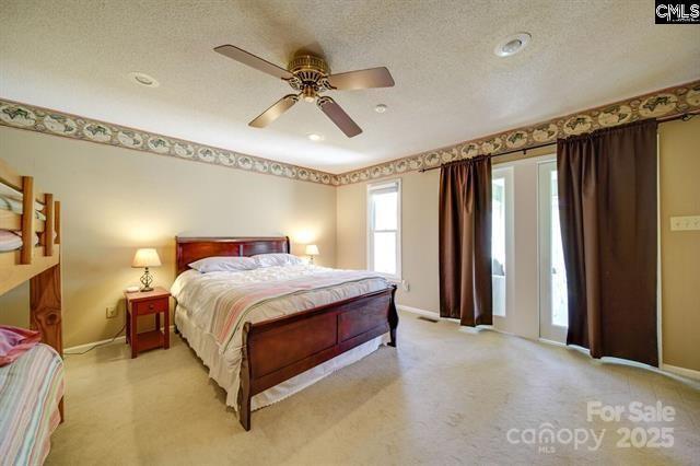 bedroom with a textured ceiling, light carpet, a ceiling fan, and baseboards