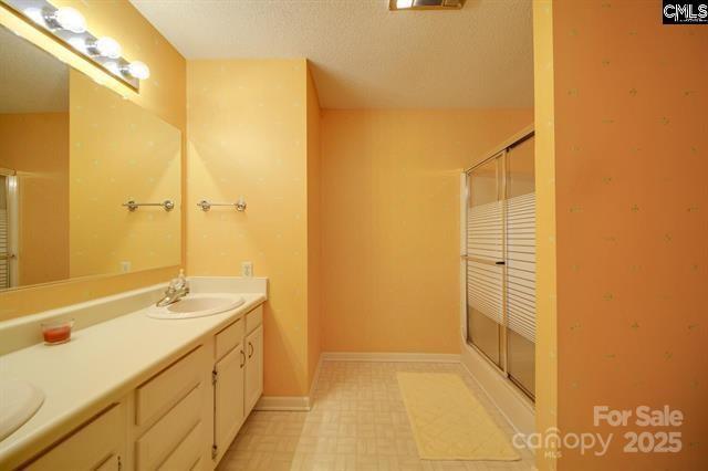 full bathroom featuring a stall shower, a sink, baseboards, and double vanity