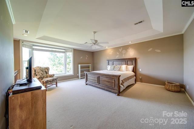 bedroom with light carpet, visible vents, baseboards, ornamental molding, and a tray ceiling