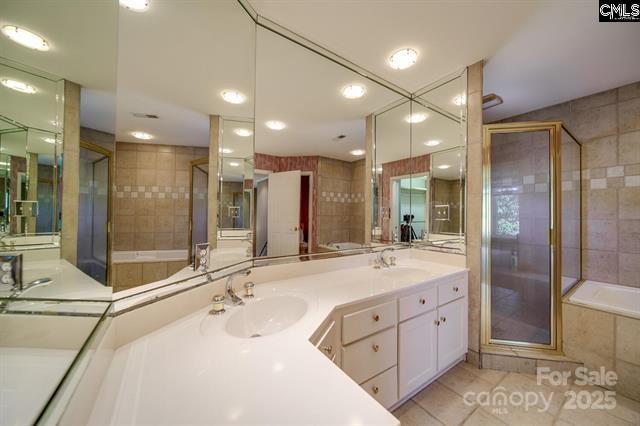 bathroom with double vanity, a stall shower, a garden tub, and a sink