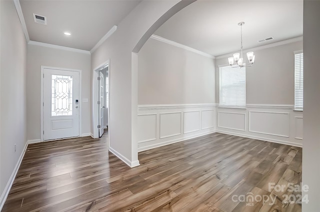 entryway with wood-type flooring, an inviting chandelier, plenty of natural light, and crown molding