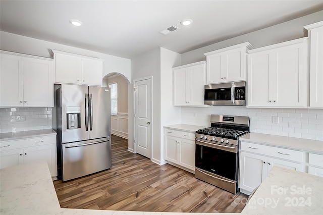 kitchen with decorative backsplash, appliances with stainless steel finishes, light stone countertops, wood-type flooring, and white cabinets