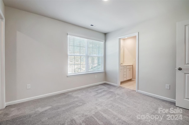 unfurnished bedroom featuring light carpet and ensuite bath