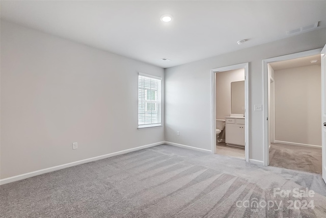 unfurnished bedroom featuring ensuite bathroom and light colored carpet