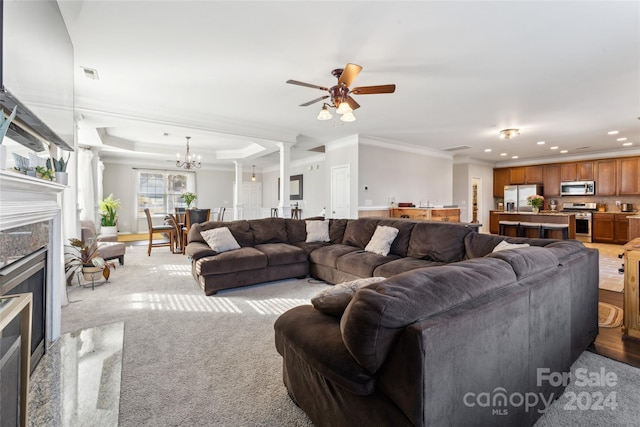 carpeted living room featuring a fireplace, ceiling fan with notable chandelier, a raised ceiling, and crown molding