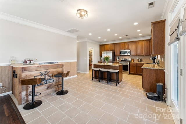 kitchen with light stone counters, ornamental molding, a breakfast bar, stainless steel appliances, and a center island