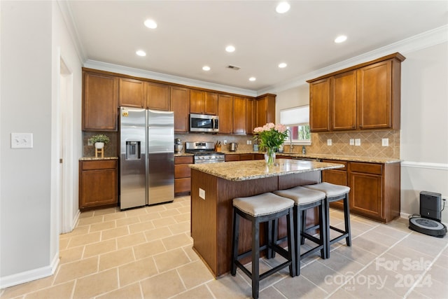 kitchen featuring appliances with stainless steel finishes, a kitchen breakfast bar, tasteful backsplash, light stone counters, and a center island