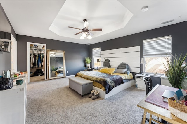 carpeted bedroom with a tray ceiling, a spacious closet, a closet, and ceiling fan