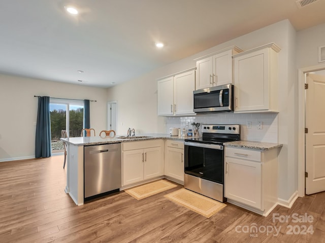 kitchen featuring kitchen peninsula, appliances with stainless steel finishes, sink, light hardwood / wood-style flooring, and white cabinetry