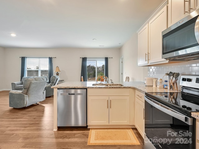 kitchen with light stone countertops, sink, stainless steel appliances, light hardwood / wood-style floors, and decorative backsplash