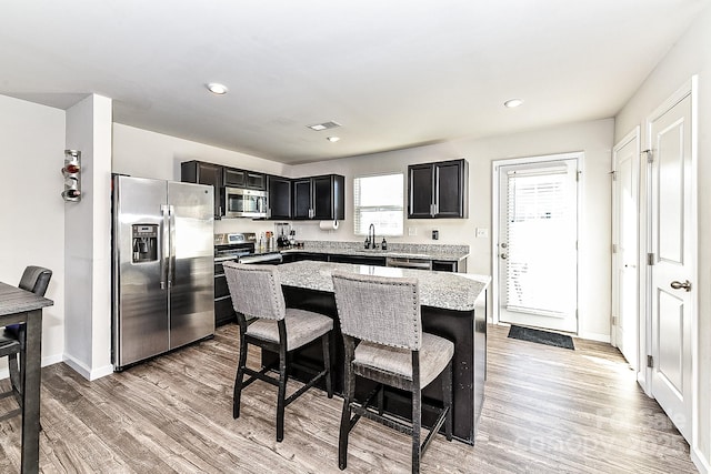 kitchen featuring a center island, light stone countertops, light hardwood / wood-style floors, a kitchen bar, and stainless steel appliances