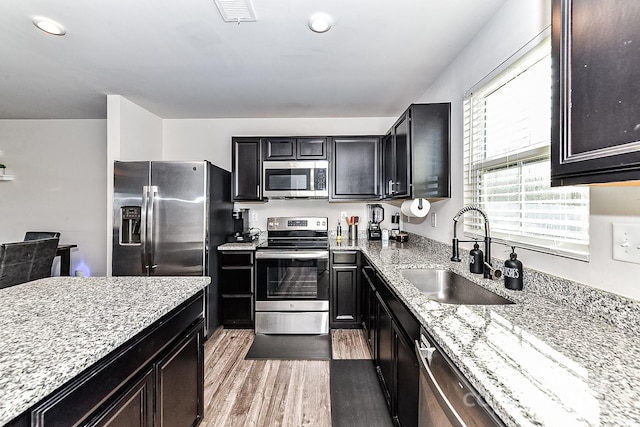 kitchen with light stone countertops, sink, wood-type flooring, and appliances with stainless steel finishes