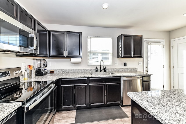 kitchen with light stone counters, sink, stainless steel appliances, and light hardwood / wood-style flooring