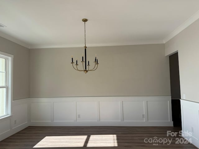 unfurnished dining area featuring dark wood-type flooring, a chandelier, and ornamental molding