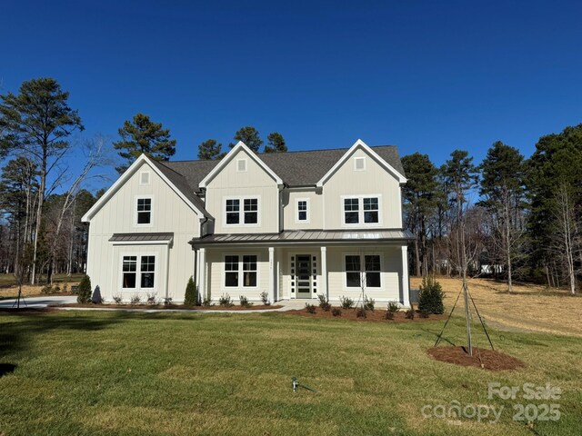 modern farmhouse style home with roof with shingles, a standing seam roof, a porch, board and batten siding, and a front yard