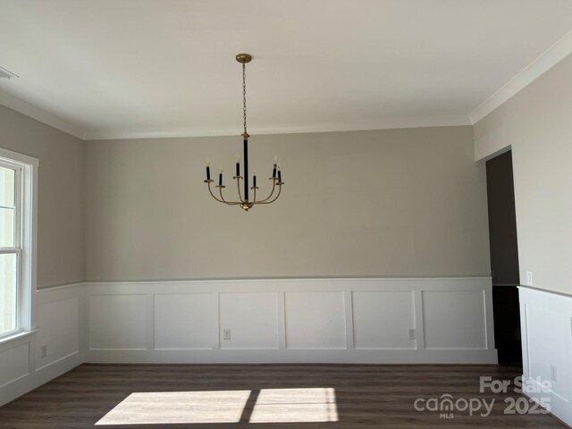 unfurnished dining area featuring a wainscoted wall, visible vents, ornamental molding, dark wood-style floors, and an inviting chandelier