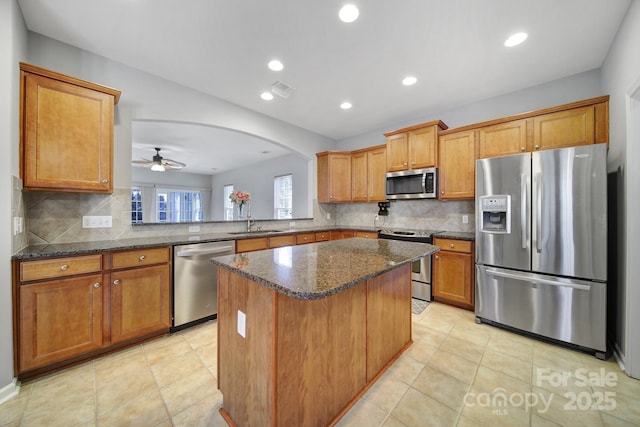 kitchen featuring kitchen peninsula, appliances with stainless steel finishes, dark stone counters, ceiling fan, and sink