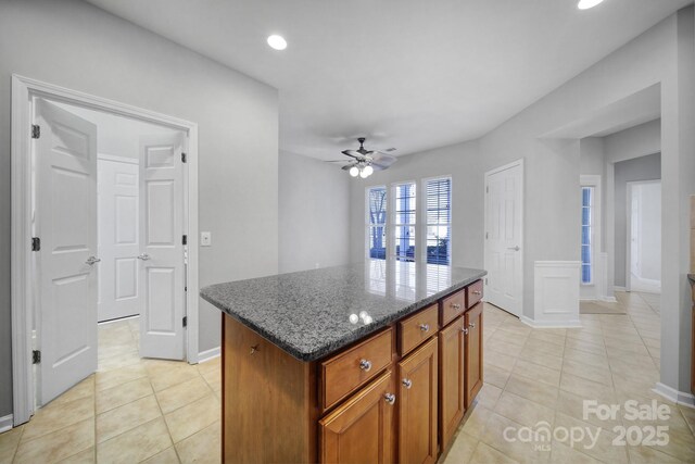 kitchen featuring ceiling fan, a center island, light tile patterned flooring, and dark stone counters