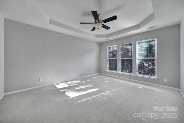 empty room with light carpet, a tray ceiling, and ceiling fan