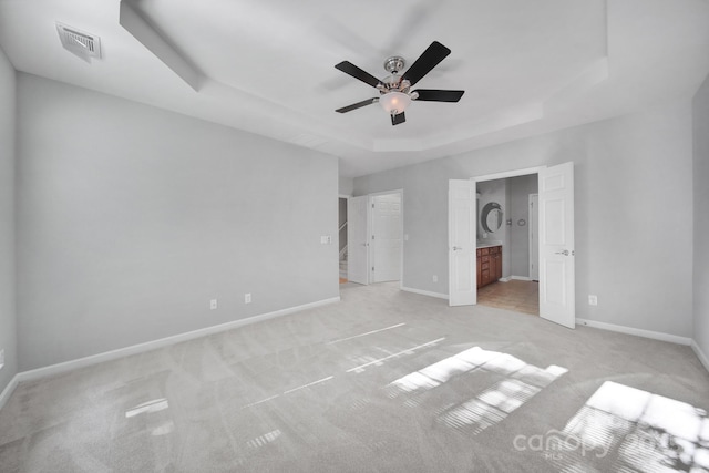 unfurnished bedroom with a tray ceiling, ceiling fan, light colored carpet, and ensuite bathroom