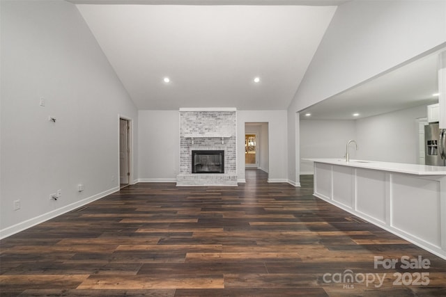 unfurnished living room with high vaulted ceiling, a brick fireplace, dark hardwood / wood-style floors, and sink