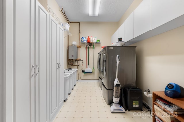 laundry room featuring cabinets, a textured ceiling, washer and clothes dryer, and water heater