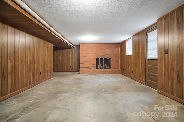 unfurnished living room featuring wood walls, a textured ceiling, and a brick fireplace