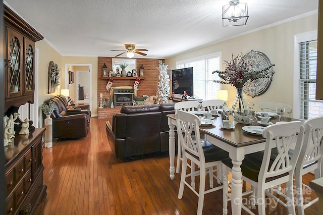 dining space with dark wood finished floors, ceiling fan, crown molding, a textured ceiling, and a fireplace