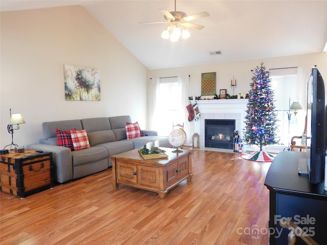 living room featuring ceiling fan, vaulted ceiling, a tile fireplace, and light wood-type flooring