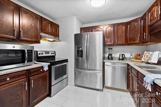 kitchen featuring dark brown cabinetry, sink, a textured ceiling, light tile patterned floors, and appliances with stainless steel finishes