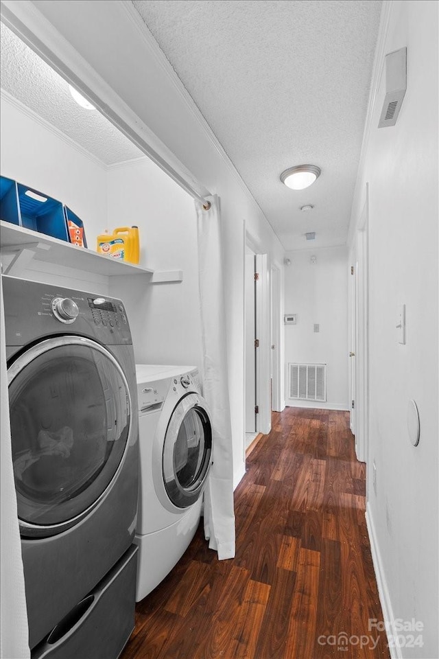 clothes washing area featuring washing machine and dryer, dark hardwood / wood-style floors, a textured ceiling, and ornamental molding