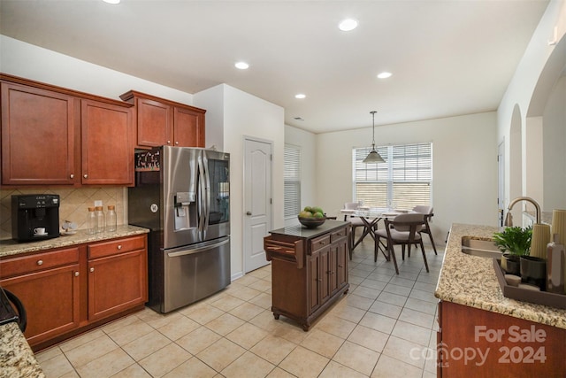 kitchen featuring light stone countertops, stainless steel fridge, tasteful backsplash, sink, and pendant lighting