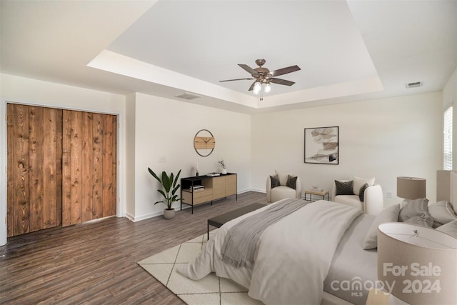 bedroom featuring a tray ceiling, ceiling fan, a closet, and dark wood-type flooring