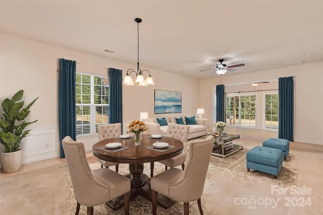 carpeted dining area with ceiling fan with notable chandelier and a healthy amount of sunlight