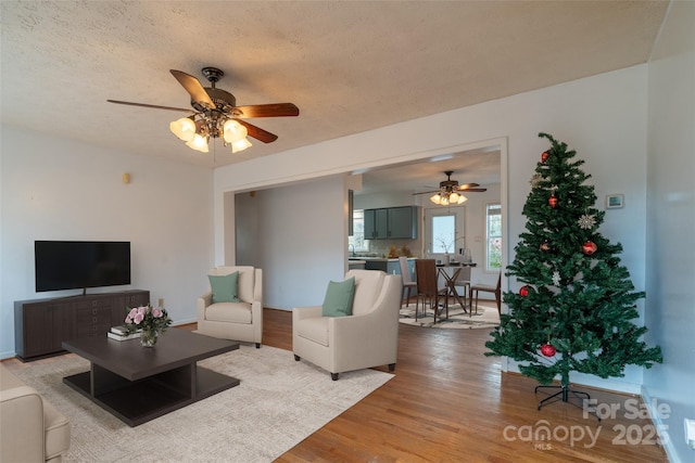 living room with a textured ceiling, light wood-type flooring, and ceiling fan